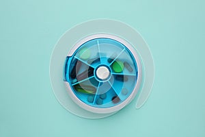 Plastic box with different pills on blue background, top view