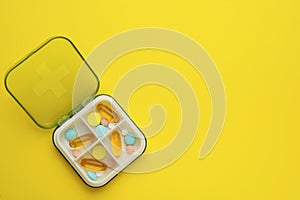 Plastic box with different pills on yellow, top view. Space for text