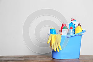 Plastic bucket with different cleaning products on table against light background