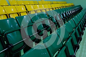 Plastic chairs for spectators in the gym. Auditorium with rows of raised green and yellow seats