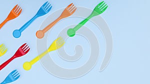 Plastic colorful forks appear from left side on blue background - Stop motion
