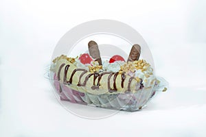 Plastic container with ice cream and bananas in it covered in chocolate and nuts