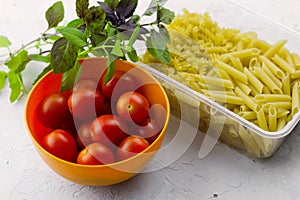 Plastic container with two types of pasta ,bowl with ripe tomatoes and fresh basil leaves