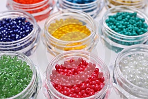 Plastic containers with different beads on white background, closeup