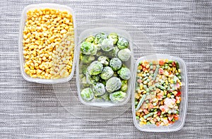 Plastic containers with frozen vegetables on grey background, top view, Different frozen vegetables on table, corn brussels