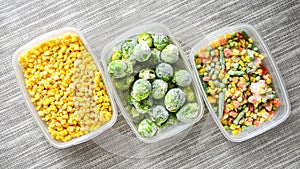 Plastic containers with frozen vegetables on grey background, top view, Different frozen vegetables on table, corn brussels