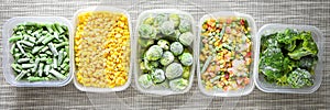 Plastic containers with frozen vegetables on grey background, top view, Different frozen vegetables on table, corn brussels