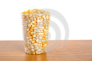 Plastic cup full of corn seeds on white