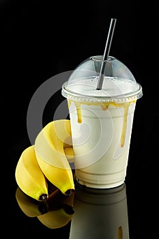 Plastic cup of milkshake with banana isolated on balck background