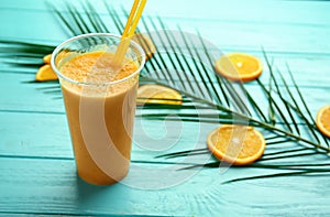 Plastic cup of tasty orange smoothie on color wooden table