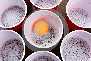 Plastic cups and ball for beer pong on wooden table, flat lay