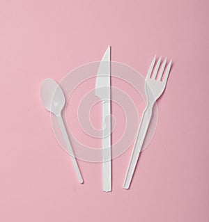 Plastic cutlery for picnics on a pink background. Disposable spoon, fork, knife. Top view, copy space