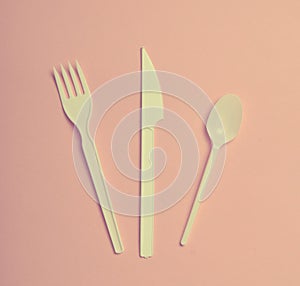 Plastic cutlery for picnics on a pink background. Disposable spoon, fork, knife. Top view, copy space..