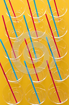 Plastic disposable cups with colored straws, Concept of reducing the amount of artificial materials on earth / yellow background