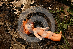 A plastic doll, dirty with soot, in front of the remains of a burnt-out house caused by a bombing raid.