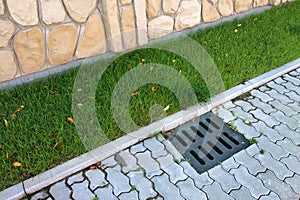 Plastic drain gutter, green grass lawn and stone pavement sidewalk