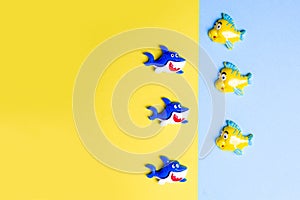 Plastic fish and shark on a blue and yellow background. Funny children`s toys made of polymer clay, flatly, copy space