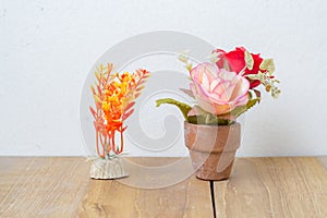 Plastic flower in pot and plastic plant on wooden board