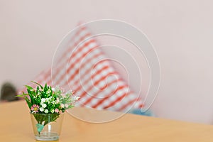 plastic flowers in glass vase on table with blur pillow backgrpound