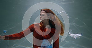 Plastic footprint. Young woman spreading waste under water, single use packaging garbage floating around slow motion.