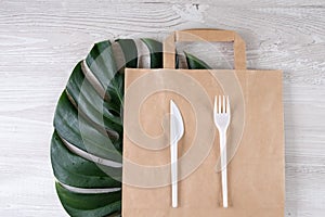 Plastic fork, knife on paper bag. Eco-friendly food packaging and cotton eco bags on gray background with copy space