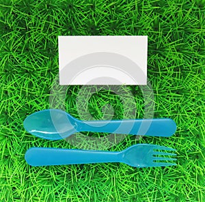 Plastic fork and spoon on a green lawn with a business card top