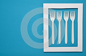 Plastic forks for picnics in a white frame on a blue background. Top view, minimalistic trend