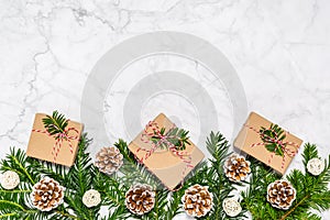 Plastic free Christmas flat lay with conifer tree branches, pine cones and handmade giftboxes on marble background. Greeting card