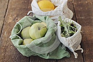 Plastic free grocery shopping. Fresh apples, lemons and arugula in eco cotton bags on rustic wood