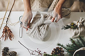 Plastic free holidays, zero waste Christmas. Hands wrapping christmas gift in linen fabric in furoshiki style on white rustic photo