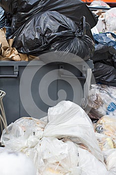 plastic garbage bags loaded with food and junk overflowing container