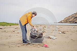 Plastic garbage. Sea and ocean pollution. Beach clean up. Young man picking used plastic bottles on sand shore