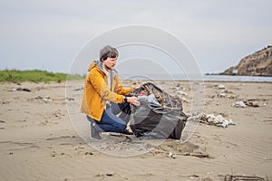 Plastic garbage. Sea and ocean pollution. Beach clean up. Young man picking used plastic bottles on sand shore