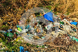 Plastic and glass bottles, bags and aluminum cans lying around among the rocks and grass. Garbage dumping in nature. The