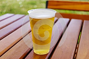 Plastic glass of light beer, standing on a wooden table, disposable glass. Cold beer