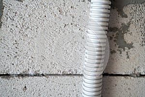 Plastic gray corrugated pipe for wiring on a close-up against the background of aerated concrete bricks