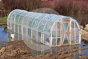 Plastic greenhouse with wooden doors surrounded with rising floodwater photo