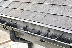 Plastic guard brush in grey plastic rain gutter on asphalt shingles roof.