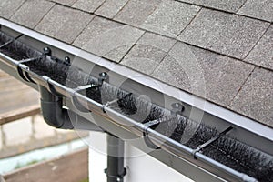 Plastic guard brush in new dark grey plastic rain gutter on asphalt shingles roof.