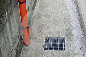 plastic gutter for collecting rainwater and the metal manhole cover of the inspectable drain in the concrete sidewalk