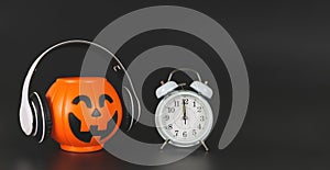 Plastic halloween pumpkin  coverd with headphones and white vintage alarm clock 12pm., isolated on black  background with copy