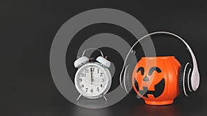 Plastic halloween pumpkin  coverd with headphones and white vintage alarm clock 12pm., isolated on black  background with copy