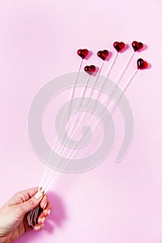 Plastic hearts on a pink background as a cluster of ballon, holding by a woman`s hand.