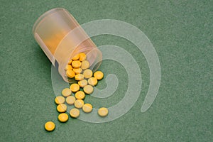 Plastic jar with yellow pills. Round yellow pills are scattered on a green background. Top view, copy space