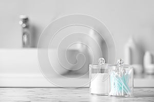 Plastic jars with cotton pads and swabs on white countertop in bathroom. Space for text