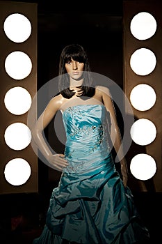 Plastic mannequin with a blue princess ball gown posing between rows of spotlights