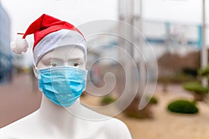 A plastic mannequin wearing a protective medical mask and red Santa hat in the shopping center -