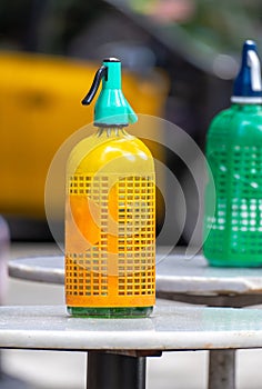 Plastic mesh siphon in orange yellow and other old and vintage green for soda on top of small round high tables on the terrace of