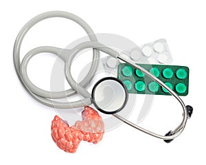 Plastic model of afflicted thyroid, pills and stethoscope on white background, top view