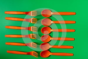 Plastic orange spoons and forks on green background